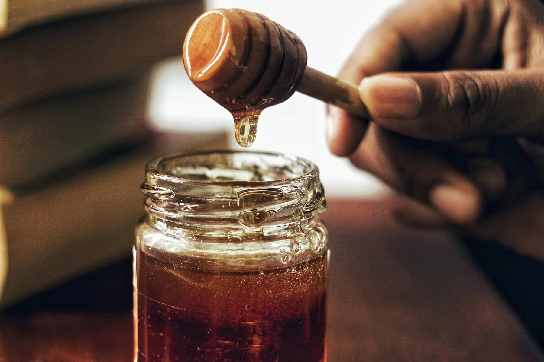 Mano tomando miel de un frasco con un cucharón de madera